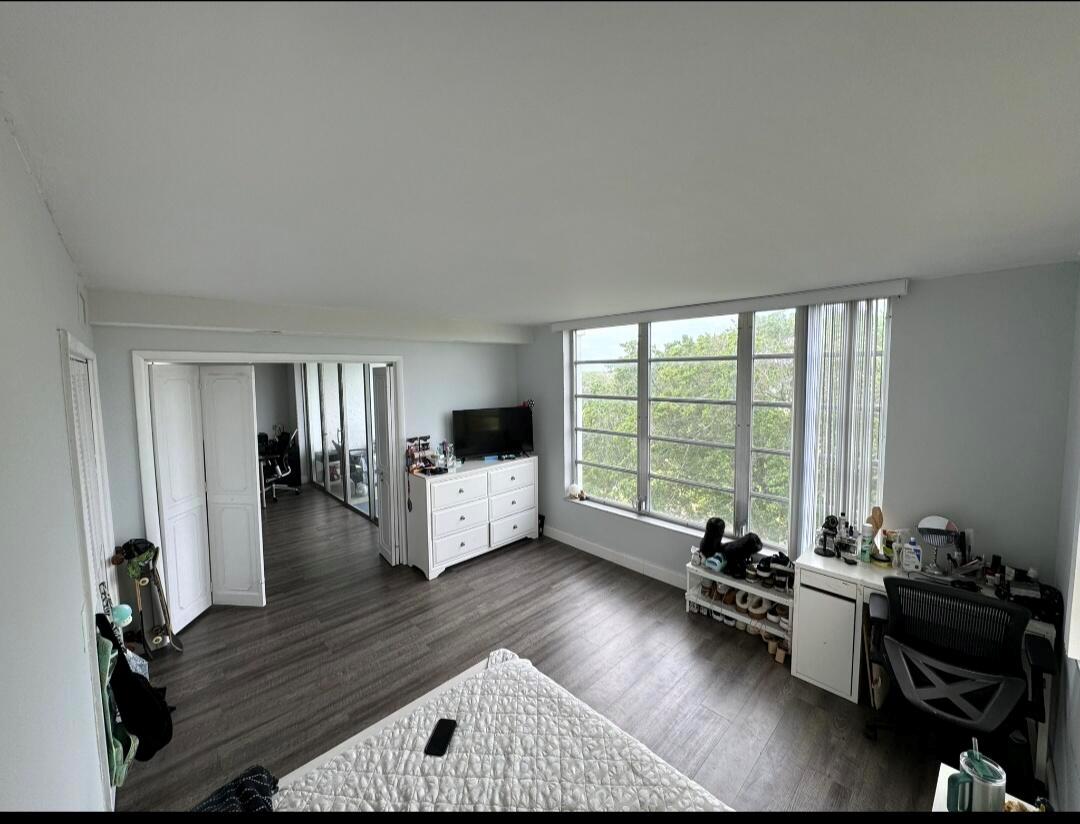 A bedroom with gray wood-look flooring, a white dresser, a desk, and large windows — 3090 N Course Drive # 601, Pompano Beach FL 33069, POMPANO BEACH, FL