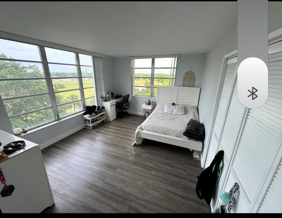 A bedroom with light gray walls, wood-look flooring, a white bed, and large corner windows — 3090 N Course Drive # 601, Pompano Beach FL 33069, POMPANO BEACH, FL