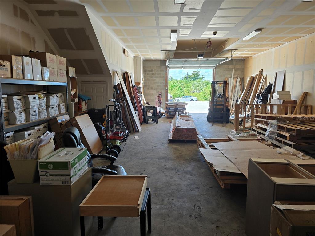 A warehouse space with concrete floors, storage shelving, stacked lumber, and an open bay door — 3131 FOLEY DRIVE UNIT 2A, PORT CHARLOTTE, FL