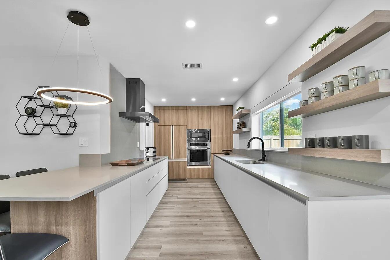 A modern kitchen features white cabinetry, wood-tone accents, stainless steel appliances, and open shelving — 803 Bluebird Drive, Delray Beach FL 33444, DELRAY BEACH, FL
