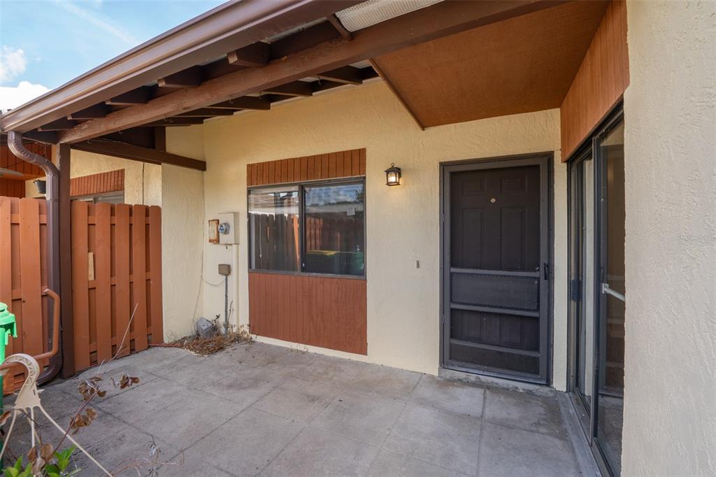 A covered concrete patio features a dark screen door, a window, and wood-paneled accents — 48 HEPBURN PLACE, MERRITT ISLAND, FL