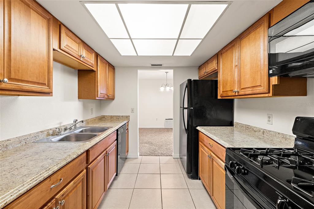 A galley kitchen features wood cabinets, granite countertops, tile flooring, and black appliances — 48 HEPBURN PLACE, MERRITT ISLAND, FL