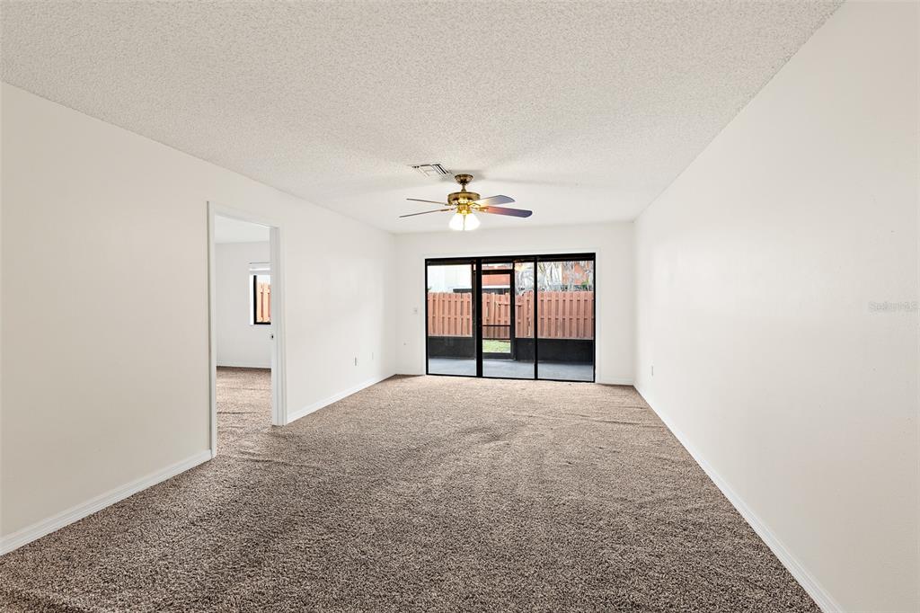 An empty living room features beige wall-to-wall carpeting, white walls, a ceiling fan, and sliding doors — 48 HEPBURN PLACE, MERRITT ISLAND, FL