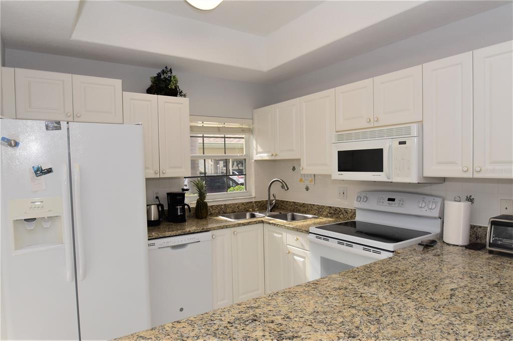 A kitchen features white cabinets, granite countertops, and white appliances — 4235 CASTLEBRIDGE LANE UNIT 1216, SARASOTA, FL
