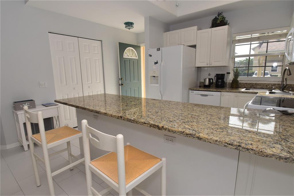 A kitchen features a granite breakfast bar, white cabinetry, and two wooden bar stools — 4235 CASTLEBRIDGE LANE UNIT 1216, SARASOTA, FL