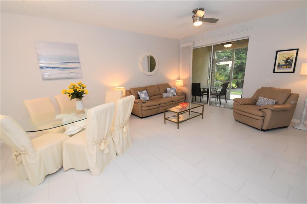 A living and dining room features white tile floors, tan furniture, and a glass sliding door — 4235 CASTLEBRIDGE LANE UNIT 1216, SARASOTA, FL