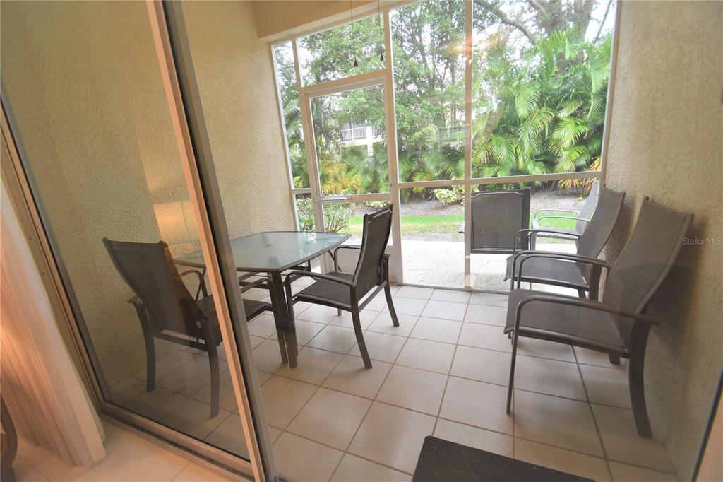 A screened-in patio features tile flooring, a glass-top dining table, and four outdoor chairs — 4235 CASTLEBRIDGE LANE UNIT 1216, SARASOTA, FL
