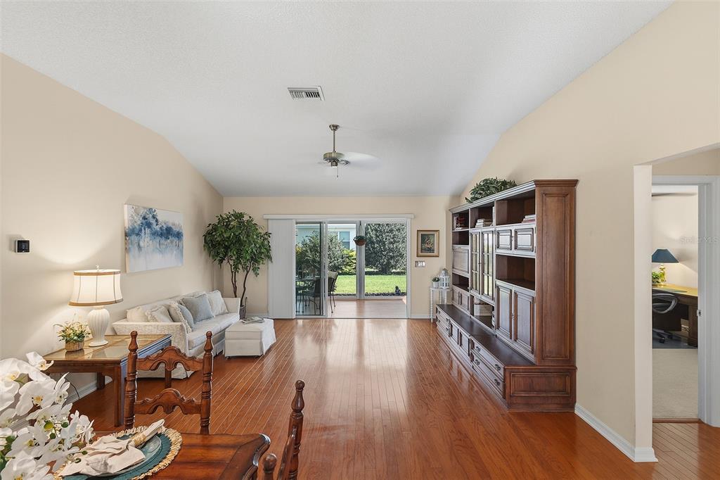 A living room with hardwood floors, a large wooden wall unit, and sliding glass doors — 1681 SHELBURNE LANE, THE VILLAGES, FL