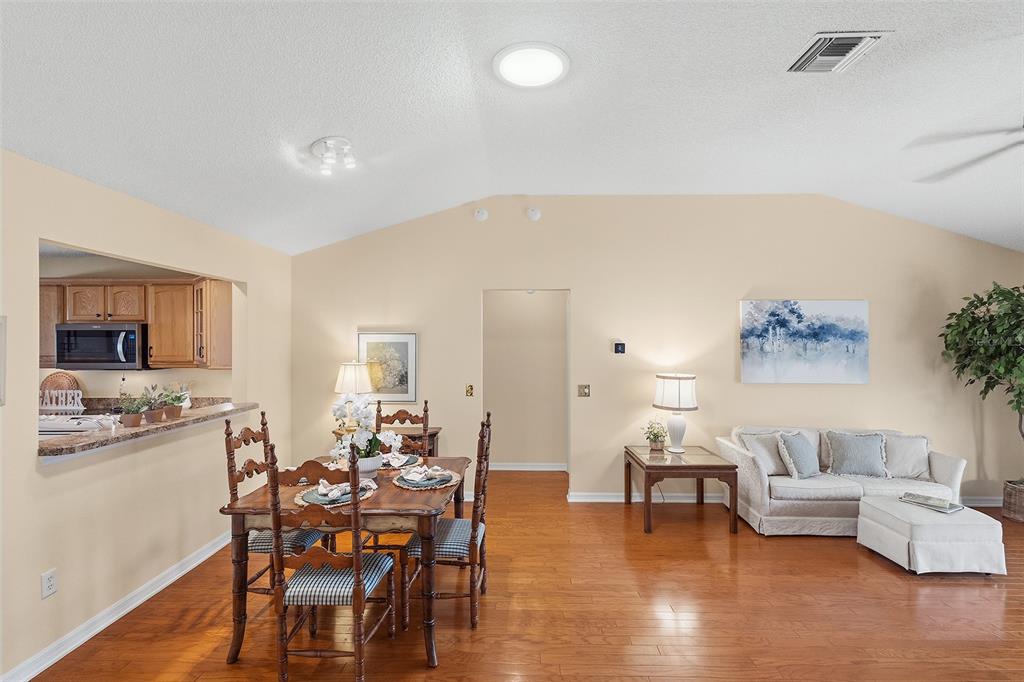 A dining area and living room feature hardwood floors, vaulted ceilings, and neutral wall paint — 1681 SHELBURNE LANE, THE VILLAGES, FL