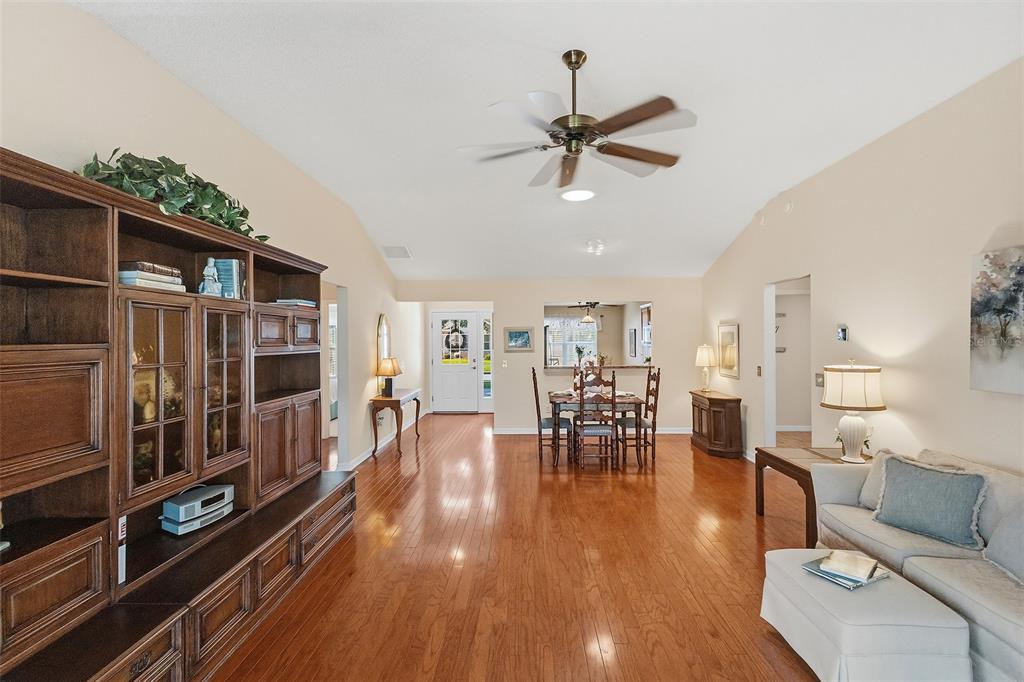 A living room with hardwood floors, a large wooden wall unit, and a dining area — 1681 SHELBURNE LANE, THE VILLAGES, FL