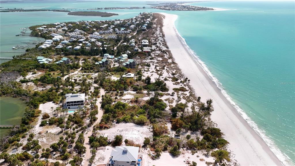 An aerial view shows a coastal community with houses, sandy terrain, and a beach — 9160 GRAND AVENUE, PLACIDA, FL