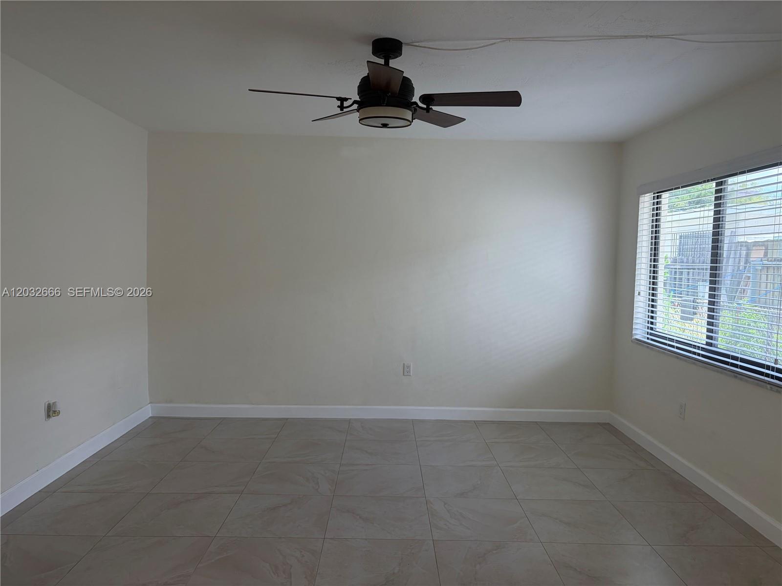 An empty room features light-colored tile flooring, a ceiling fan, and a window with blinds — 61 W 13th St # 1, Hialeah FL 33010, HIALEAH, FL