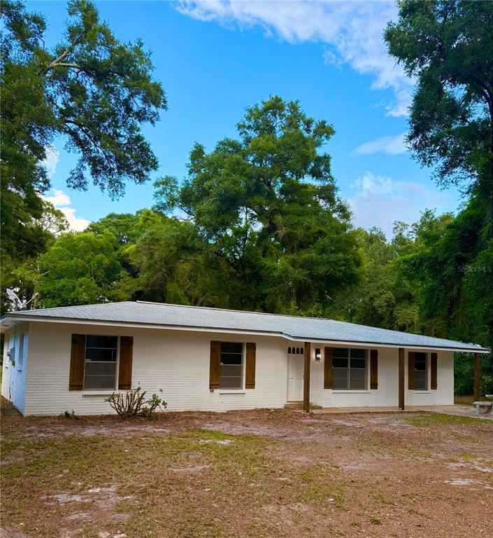 A white, single-story ranch-style house with dark shutters sits on a wooded lot — 6989 SW STATE ROAD 26, TRENTON, FL