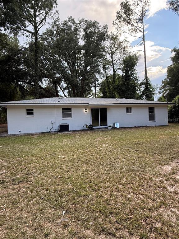The rear exterior of a single-story white house features a sliding glass door and windows — 6989 SW STATE ROAD 26, TRENTON, FL