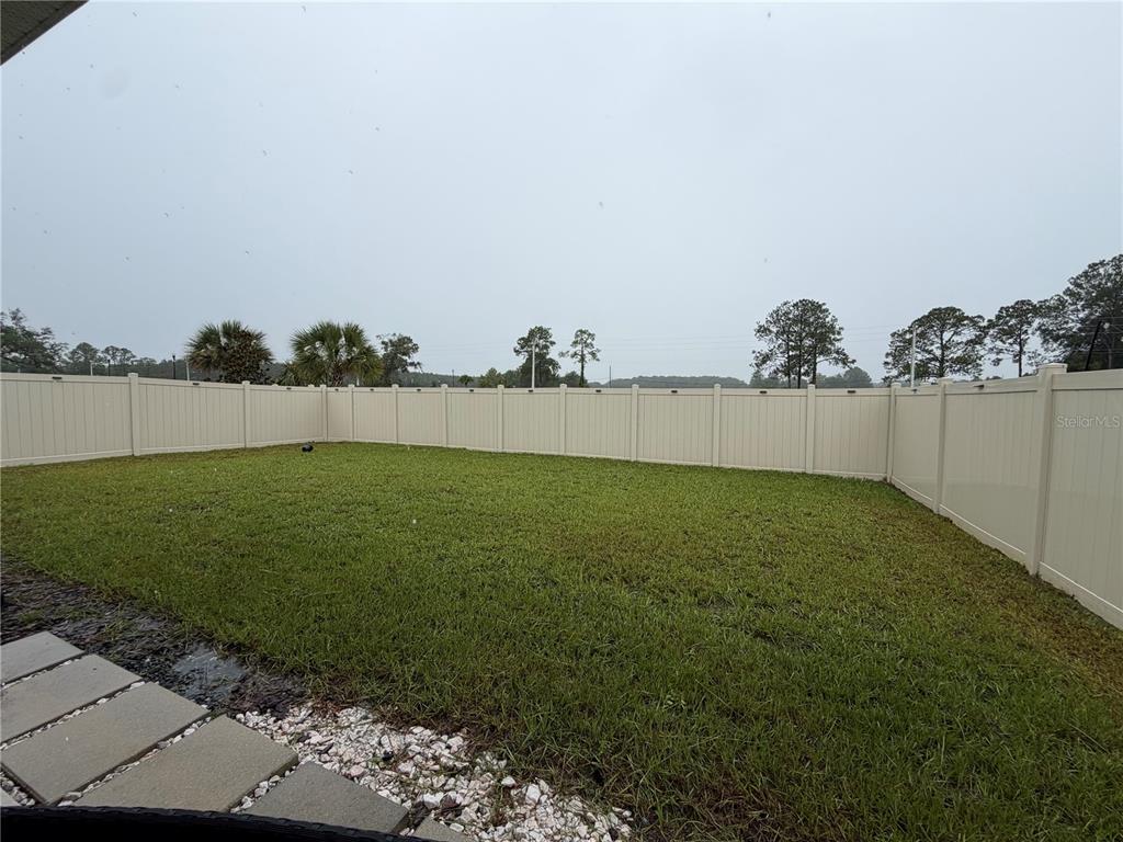 A grassy backyard enclosed by a tall, tan vinyl privacy fence under a cloudy sky — 2136 NW 248TH WAY, NEWBERRY, FL