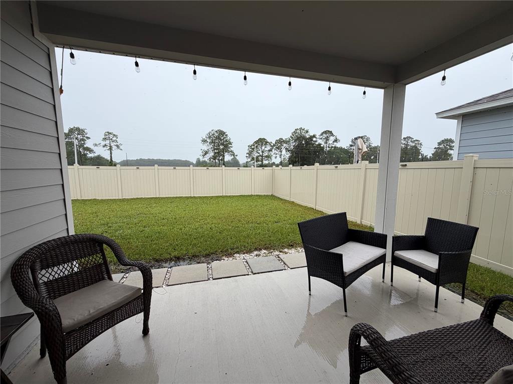 A covered concrete patio features wicker furniture and a view of a fenced backyard — 2136 NW 248TH WAY, NEWBERRY, FL