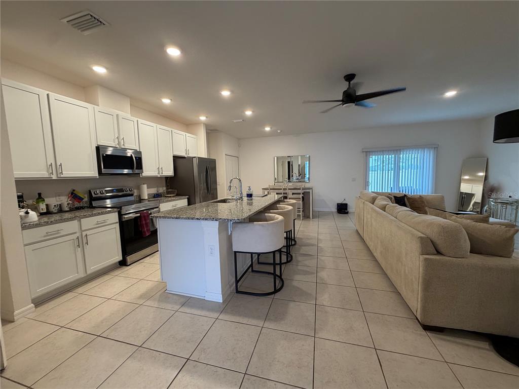 An open-concept kitchen with white cabinets, granite countertops, and an island faces a living area — 2136 NW 248TH WAY, NEWBERRY, FL