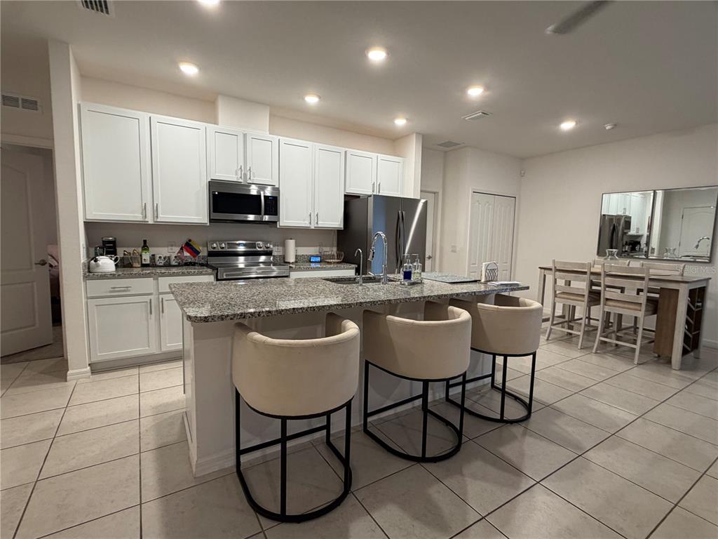 A kitchen features white cabinetry, granite countertops, a center island with bar stools, and tile flooring — 2136 NW 248TH WAY, NEWBERRY, FL