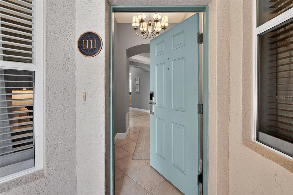 An open light blue front door reveals a tiled entryway with a chandelier inside — 35 OCEAN CREST WAY UNIT 1111, PALM COAST, FL