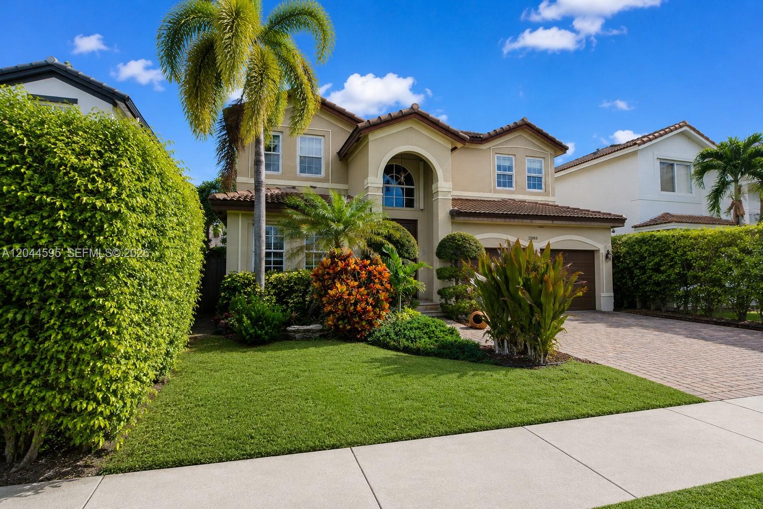 A two-story tan stucco house with a tile roof and a landscaped front yard — 13989 SW 155th Ter, Miami FL 33177, MIAMI, FL