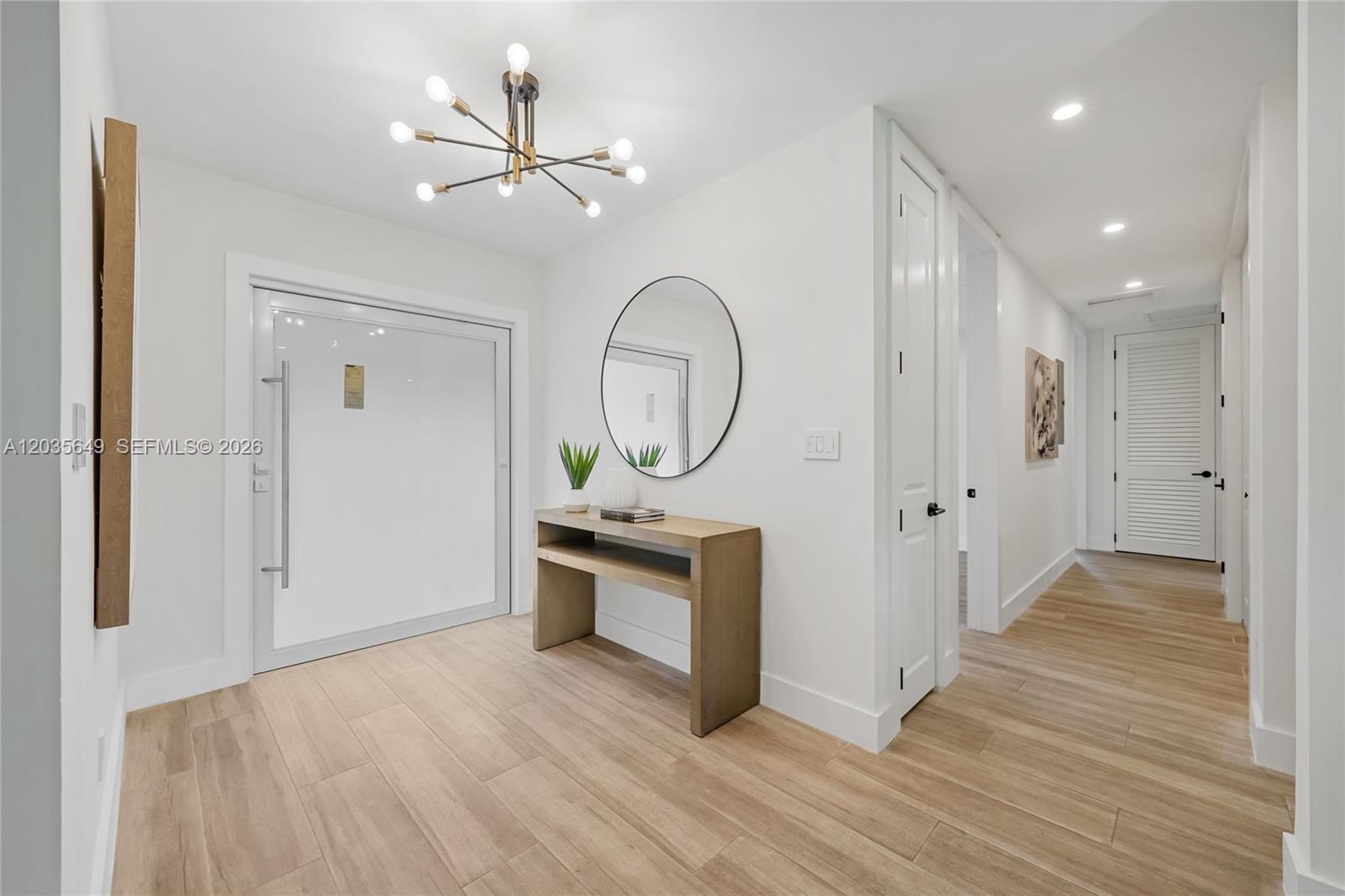 A bright entryway features a modern chandelier, a round mirror, and a wooden console table — 6600 SW 144th St, Coral Gables FL 33158, CORAL GABLES, FL