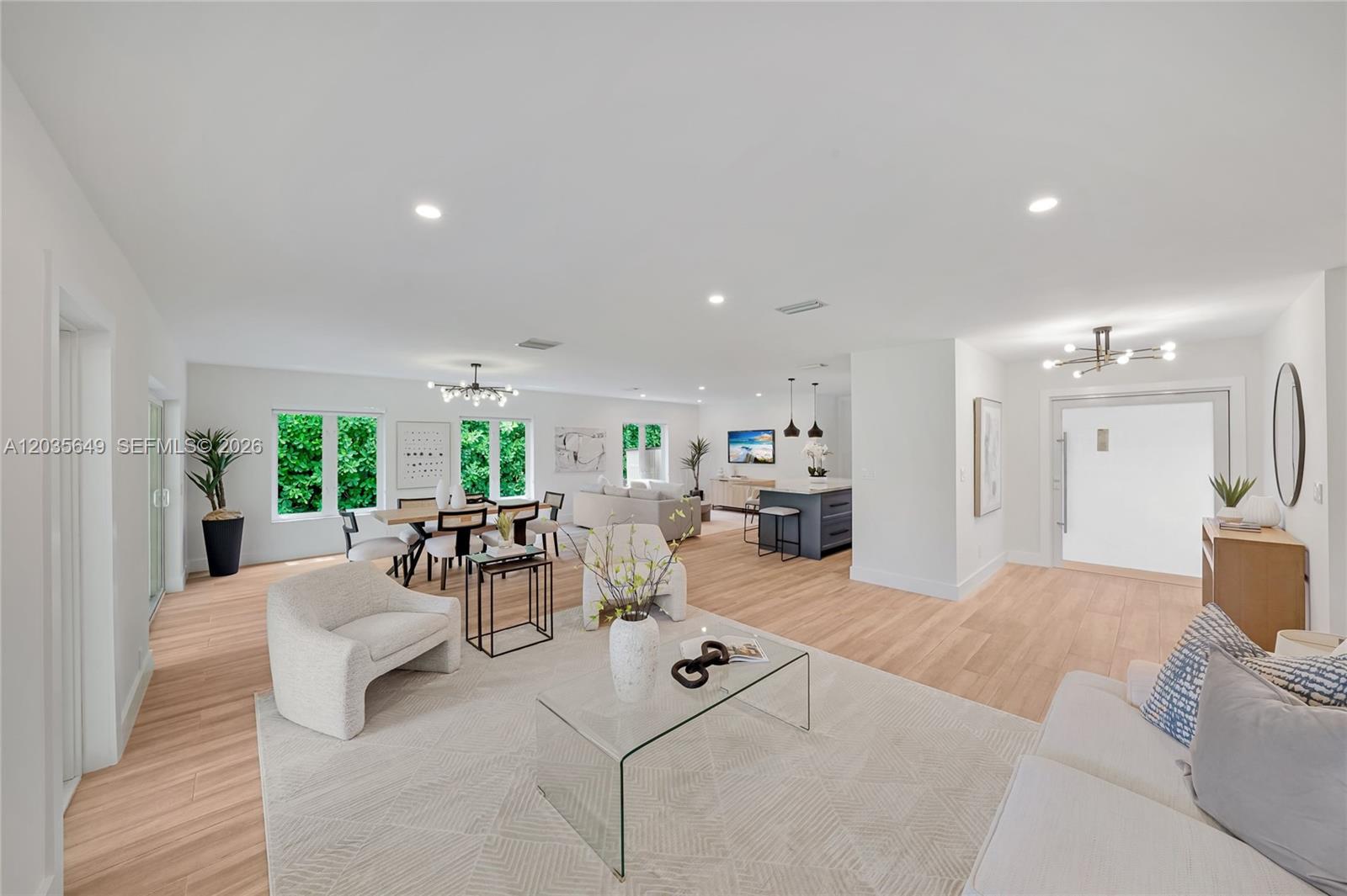 An open-concept living and dining area features light wood flooring and modern white furniture — 6600 SW 144th St, Coral Gables FL 33158, CORAL GABLES, FL