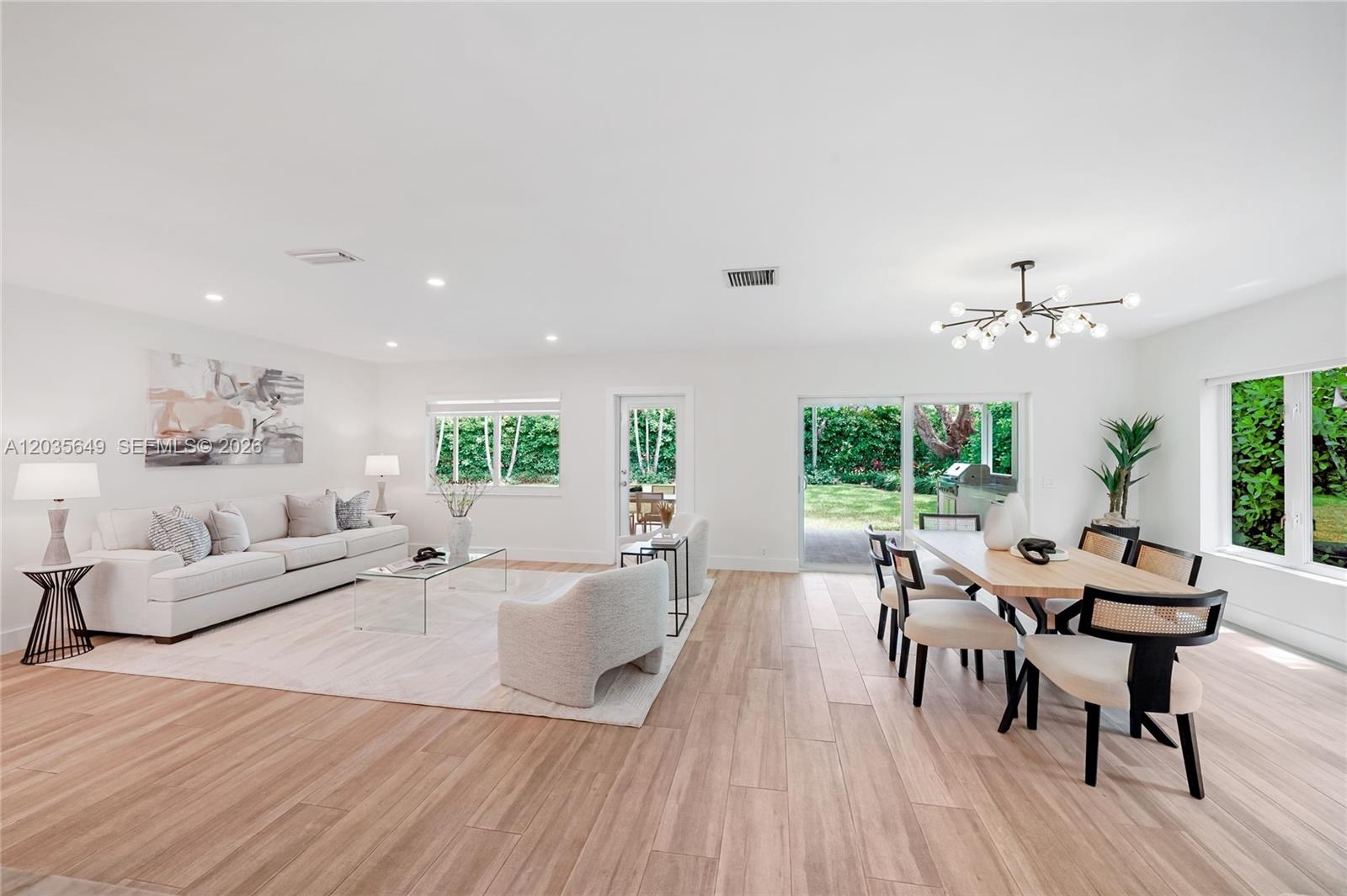 A bright, open-concept living and dining room features light wood floors and large windows — 6600 SW 144th St, Coral Gables FL 33158, CORAL GABLES, FL