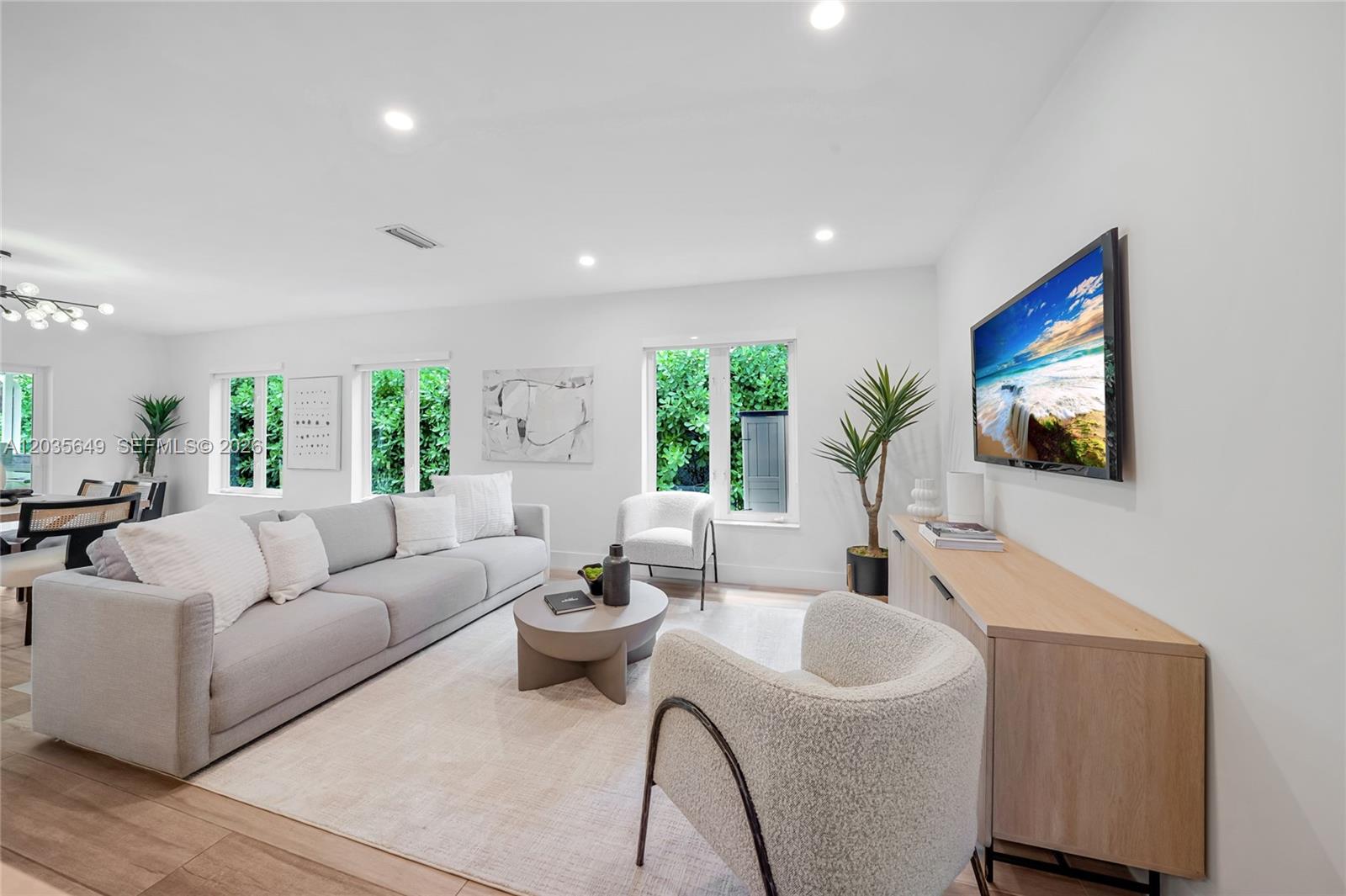 A bright living room features a grey sofa, two armchairs, a coffee table, and television — 6600 SW 144th St, Coral Gables FL 33158, CORAL GABLES, FL