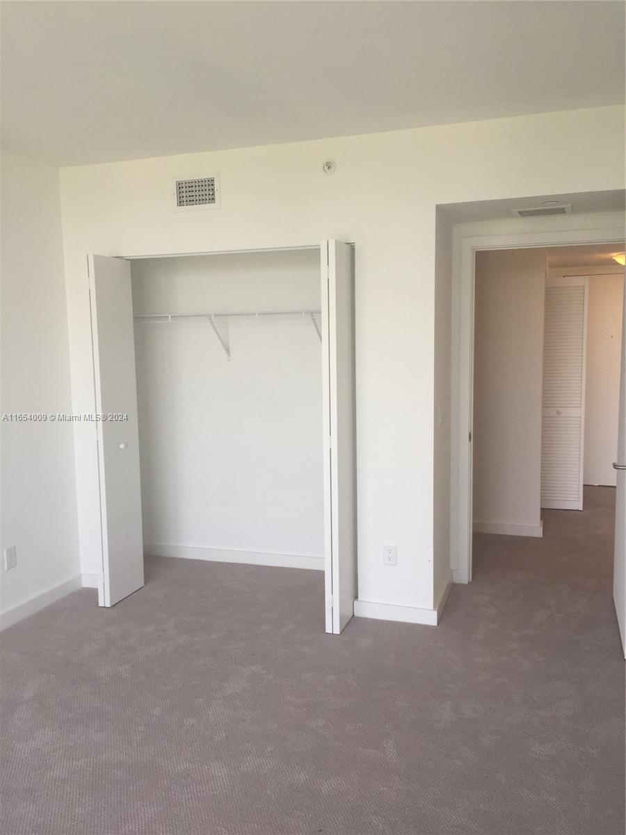 A bedroom features beige carpeting, a white closet with folding doors, and an adjacent doorway — 4250 Biscayne Blvd # 1211, Miami FL 33137, MIAMI, FL