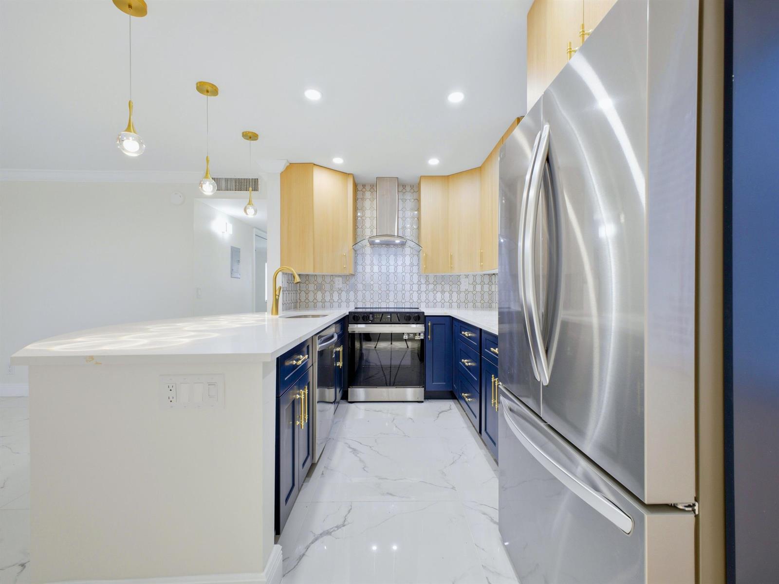 A modern kitchen features blue lower cabinets, light wood upper cabinets, and a white island — 6 Normandy A, Delray Beach FL 33484, DELRAY BEACH, FL
