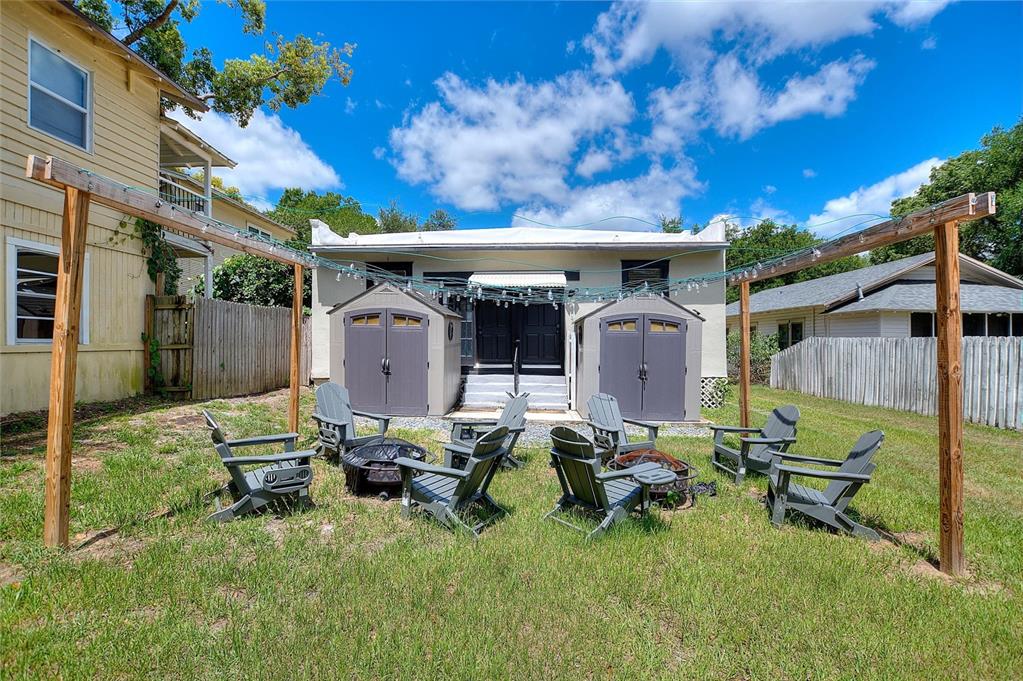 A backyard features a fire pit area with Adirondack chairs, two storage sheds, and string lights — 728 JOHNSON AVENUE, LAKELAND, FL