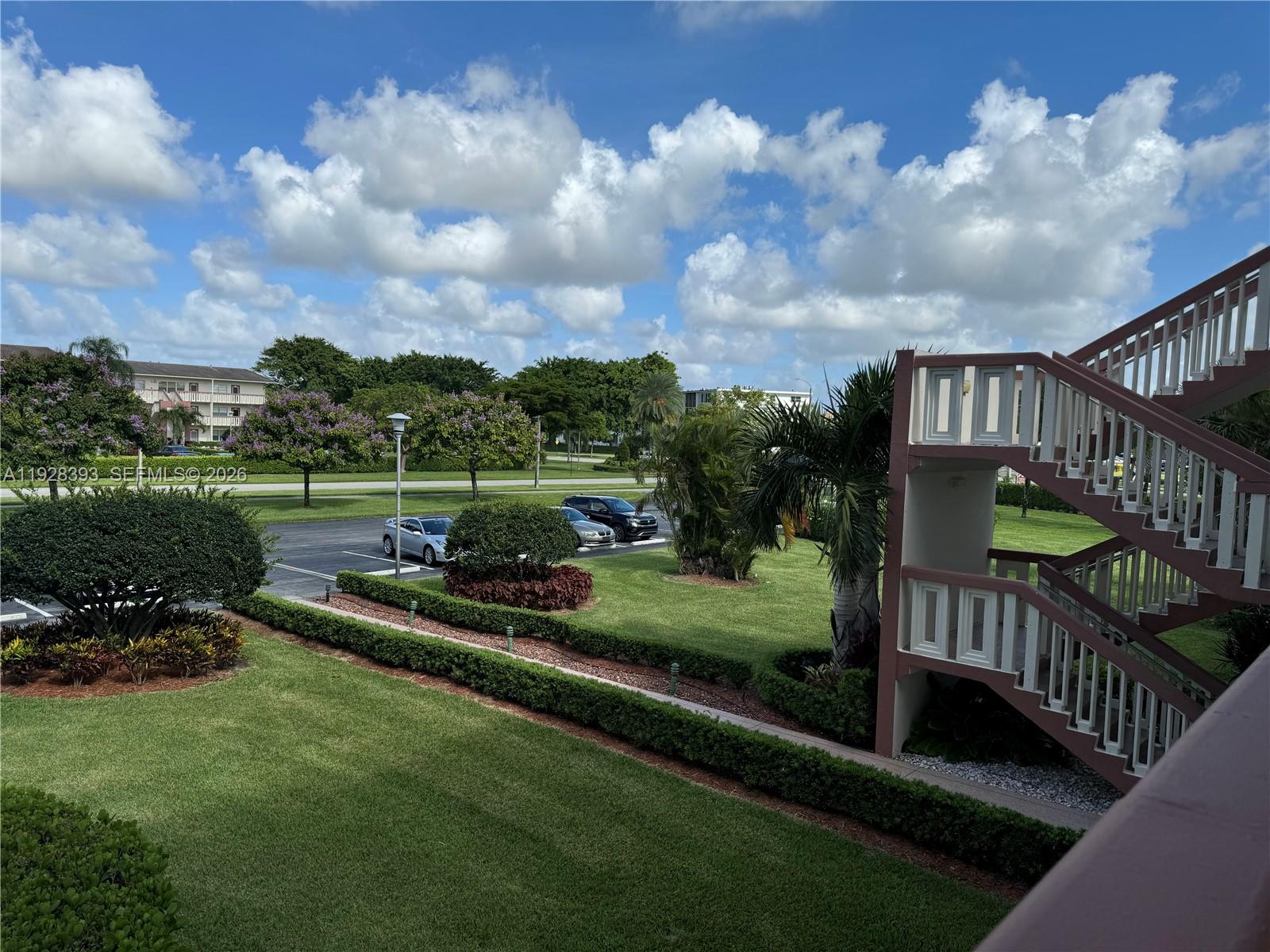 An outdoor staircase stands beside a grassy lawn with parking and trees under a cloudy sky — 149 Preston D # 149, Boca Raton FL 33434, BOCA RATON, FL