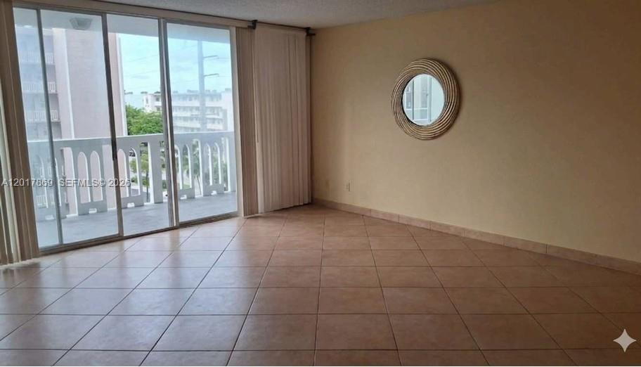 An empty room features beige tile flooring, a circular wall mirror, and sliding glass doors — 401 NE 14th Ave # 507, Hallandale Beach FL 33009, HALLANDALE BEACH, FL
