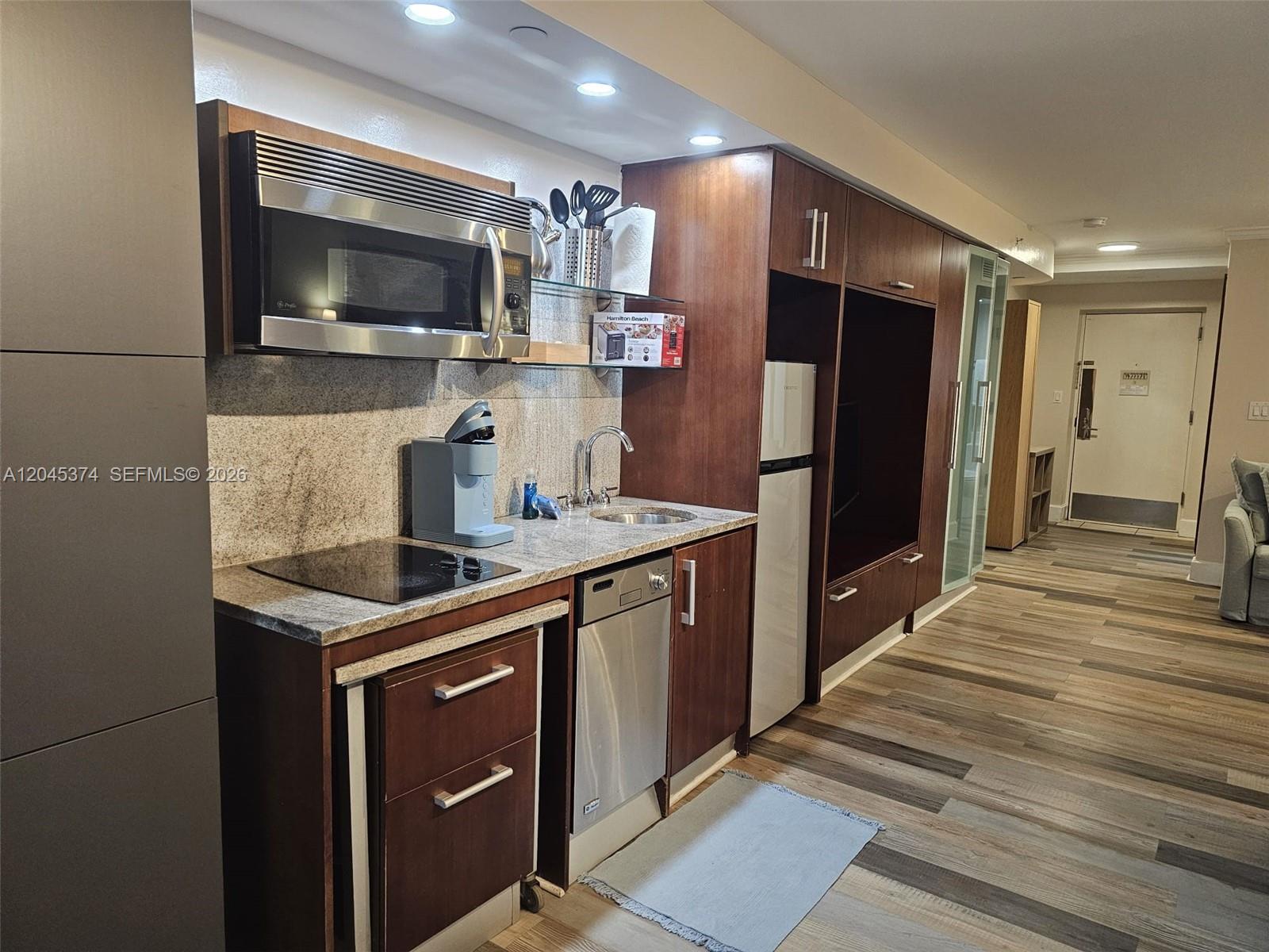 A compact kitchen features dark wood cabinetry, stainless steel appliances, and a granite countertop — 1024 Ocean Dr # A305, Miami Beach FL 33139, MIAMI BEACH, FL