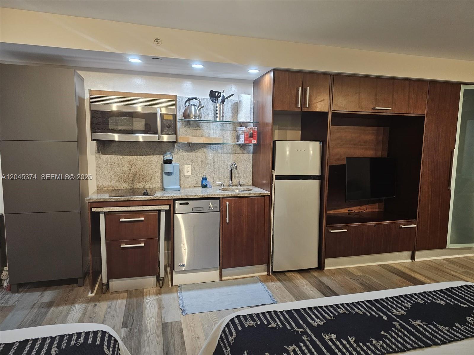 A kitchenette with wood cabinets, stainless steel appliances, and a television unit in a room — 1024 Ocean Dr # A305, Miami Beach FL 33139, MIAMI BEACH, FL