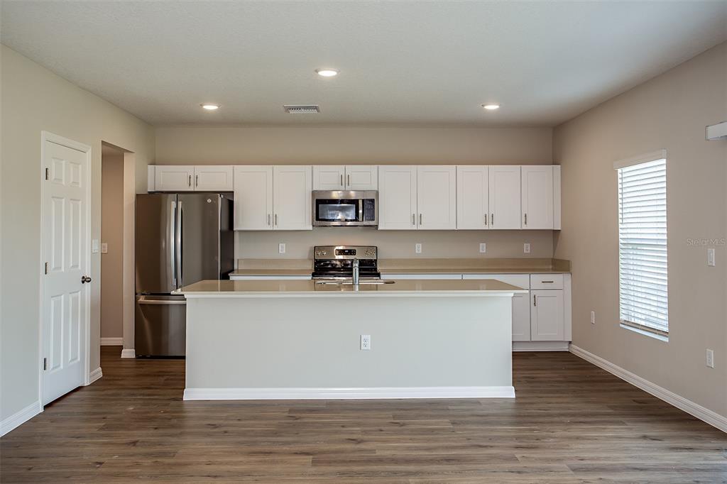 A kitchen features white cabinets, stainless steel appliances, a center island, and wood-look flooring — 5808 HEAVEN ROAD, HAINES CITY, FL