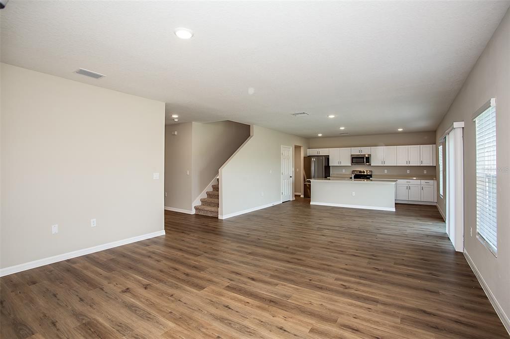 An open-concept living area features wood-look flooring, a staircase, and a kitchen with white cabinets — 5808 HEAVEN ROAD, HAINES CITY, FL