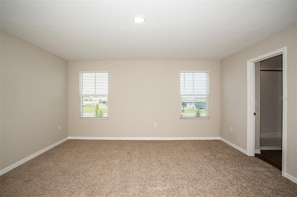 An empty bedroom features beige carpet, light-colored walls, two windows, and an open doorway — 5808 HEAVEN ROAD, HAINES CITY, FL