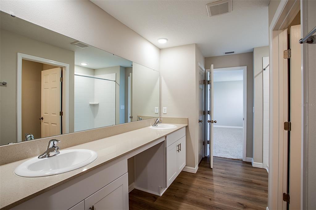 A bathroom features a long vanity with dual sinks, white cabinets, and wood-look flooring — 5808 HEAVEN ROAD, HAINES CITY, FL
