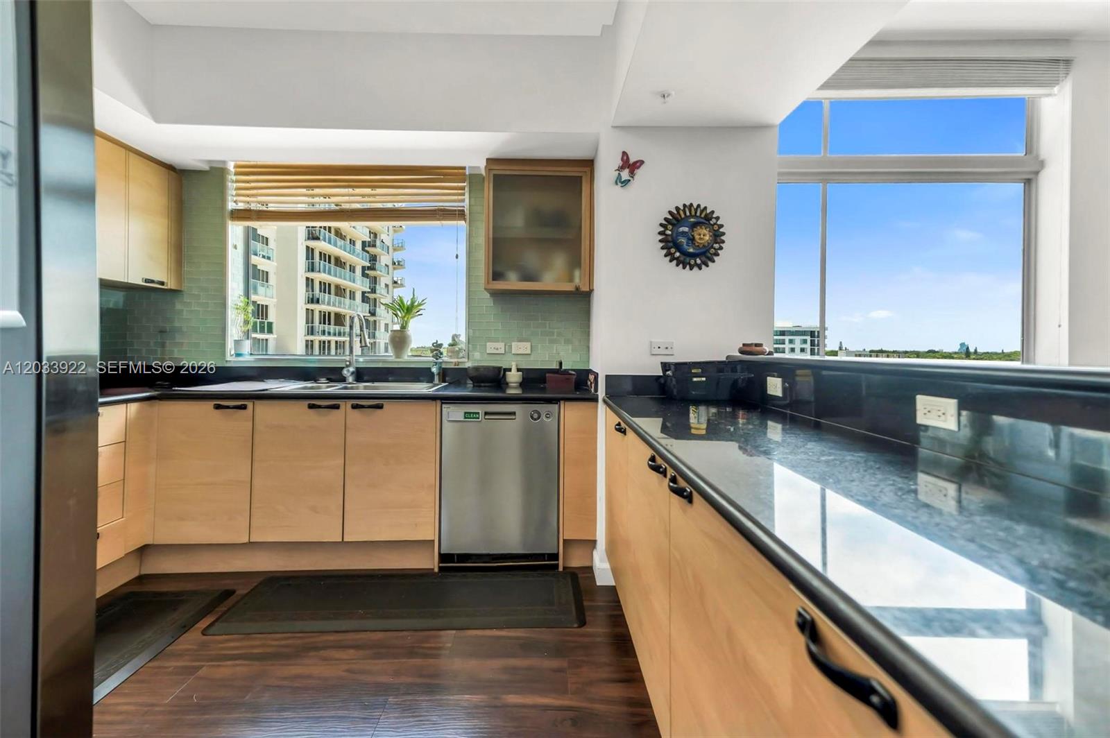 A kitchen features light wood cabinets, black countertops, a green tile backsplash, and large windows — 140 S Dixie Hwy # 501, Hollywood FL 33020, HOLLYWOOD, FL