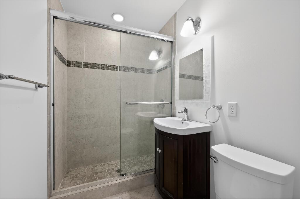 A bathroom features a glass-enclosed shower with pebble flooring, a dark wood vanity, and toilet — 636 Kingfish Road, North Palm Beach FL 33408, NORTH PALM BEACH, FL