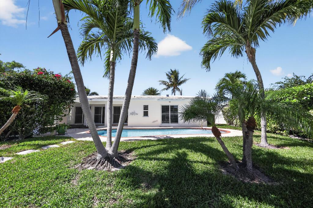 A backyard features a swimming pool, palm trees, and a white house under a blue sky — 636 Kingfish Road, North Palm Beach FL 33408, NORTH PALM BEACH, FL