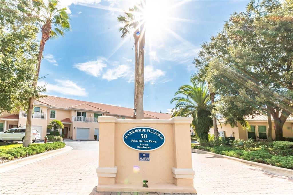 A beige stone monument sign stands at the entrance of a residential complex with palm trees — 50 PALM HARBOR PARKWAY UNIT 32, PALM COAST, FL