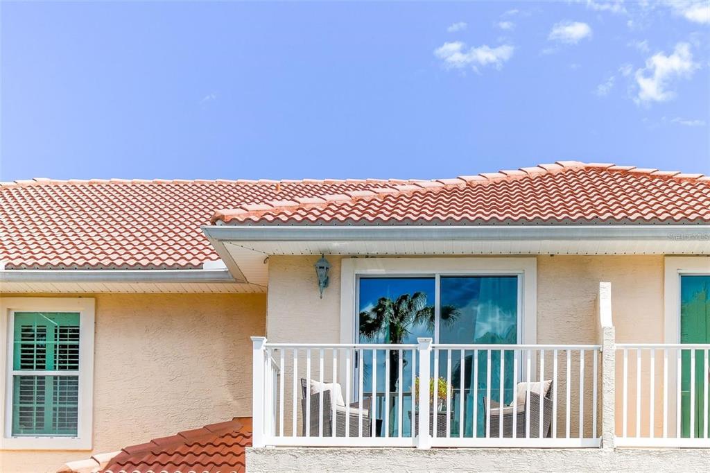 A balcony with white railings and two chairs sits beneath a tiled roof — 50 PALM HARBOR PARKWAY UNIT 32, PALM COAST, FL