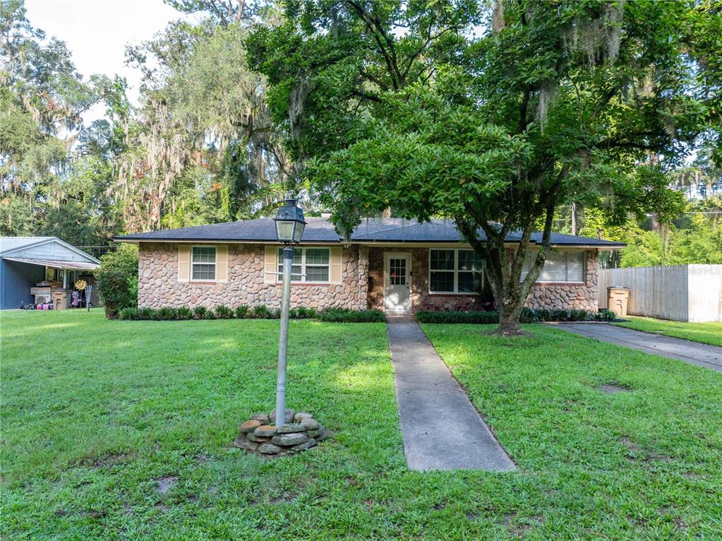 A single-story stone house with a front walkway, a lamp post, and a large tree — 1443 SE VALE COURT, LAKE CITY, FL