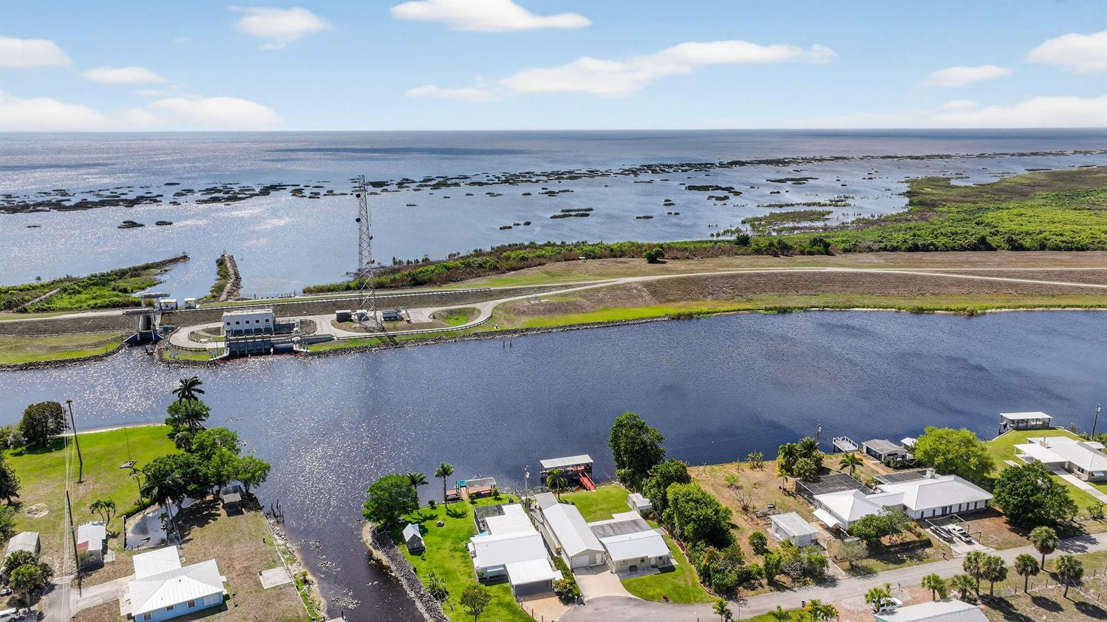 An aerial view shows houses along a canal leading to a large lake with a dam — 9700 SW Conners Highway, Okeechobee FL 34974, OKEECHOBEE, FL