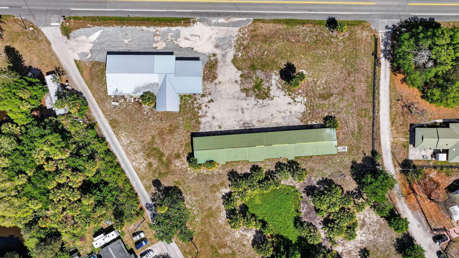Aerial view of a property featuring two buildings, a large dirt lot, and surrounding trees — 9700 SW Conners Highway, Okeechobee FL 34974, OKEECHOBEE, FL