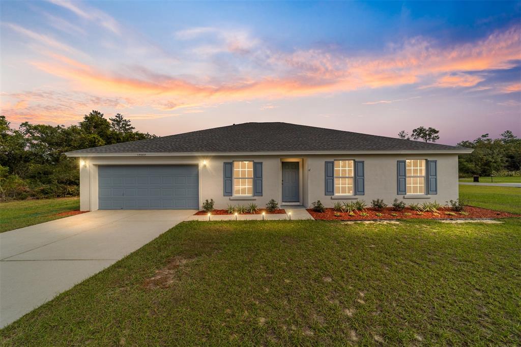 A single-story house with a gray garage, blue shutters, and a lawn at sunset — 13029 SW 35TH AVENUE ROAD, OCALA, FL