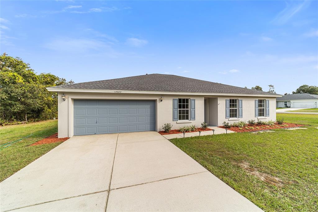 A single-story house with a gray garage door, blue shutters, and a concrete driveway — 13029 SW 35TH AVENUE ROAD, OCALA, FL