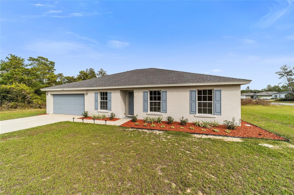 A single-story house with a light-colored stucco exterior, blue shutters, and a two-car garage — 13029 SW 35TH AVENUE ROAD, OCALA, FL